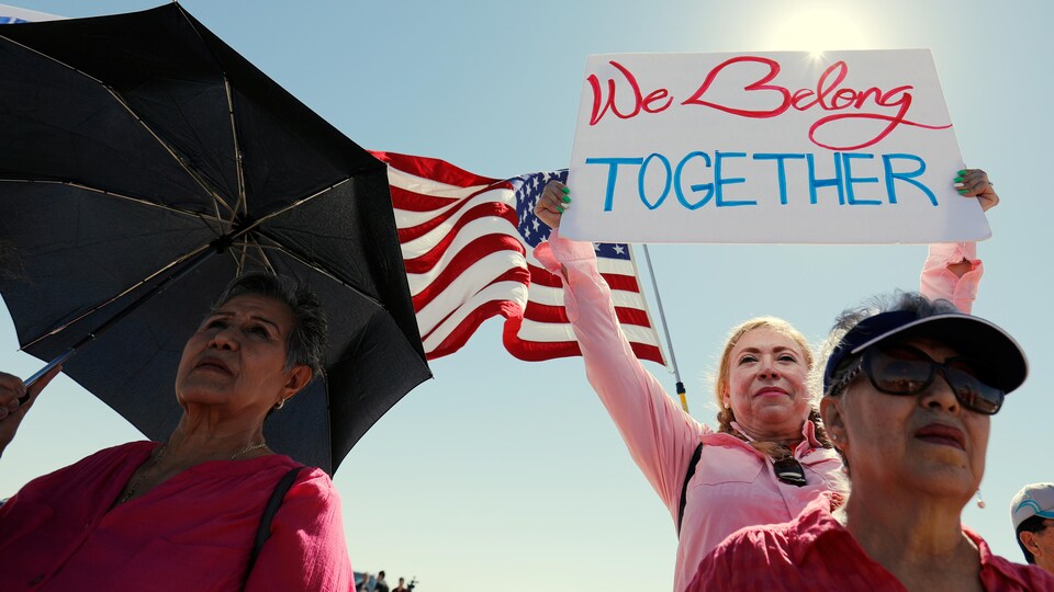 Une femme tient une affiche avec le message « Nous appartenons tous à la même communauté » en marge d'une rencontre entre des maires d'un peu partout aux États-Unis, jeudi, près d'un centre de détention d'enfants migrants à Tornillo au Texas.