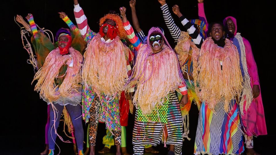 Des personnes habillées avec des vêtements très colorés dansent sur scène. 