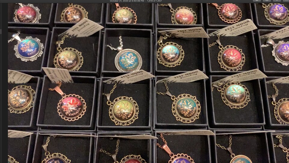 Plusieurs pendentifs créés avec de la monnaie sont exposés dans de petites boîtes.