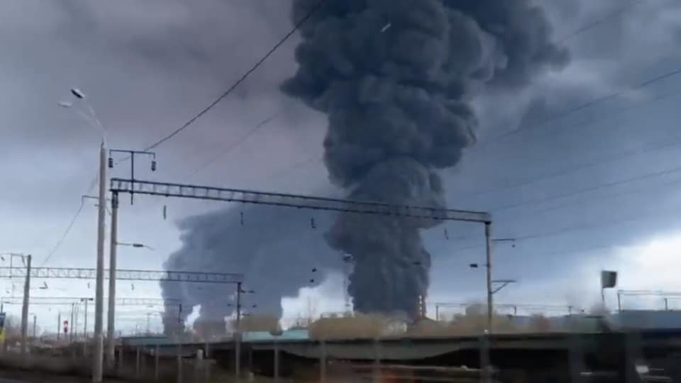 De grandes colonnes de fumée s'élèvent au loin derrière un train.