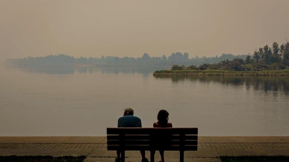 Deux personnes assises sur un banc devant un lac enfumé.