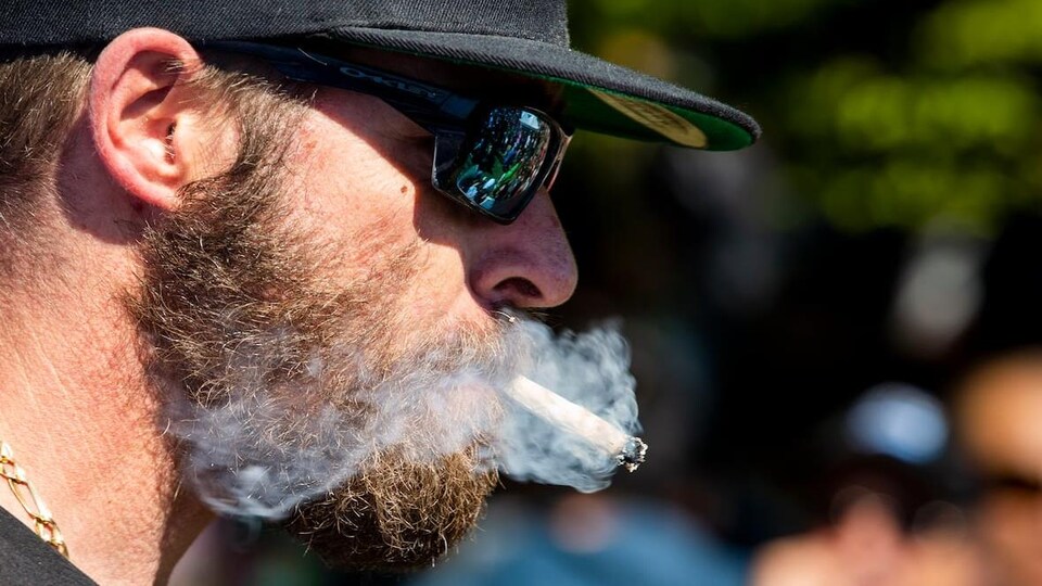 Un homme barbu fume un joint.