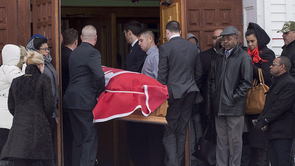 Des porteurs entrent dans l'église avec le cercueil de Lionel Desmond, recouvert d'un drapeau du Canada.
