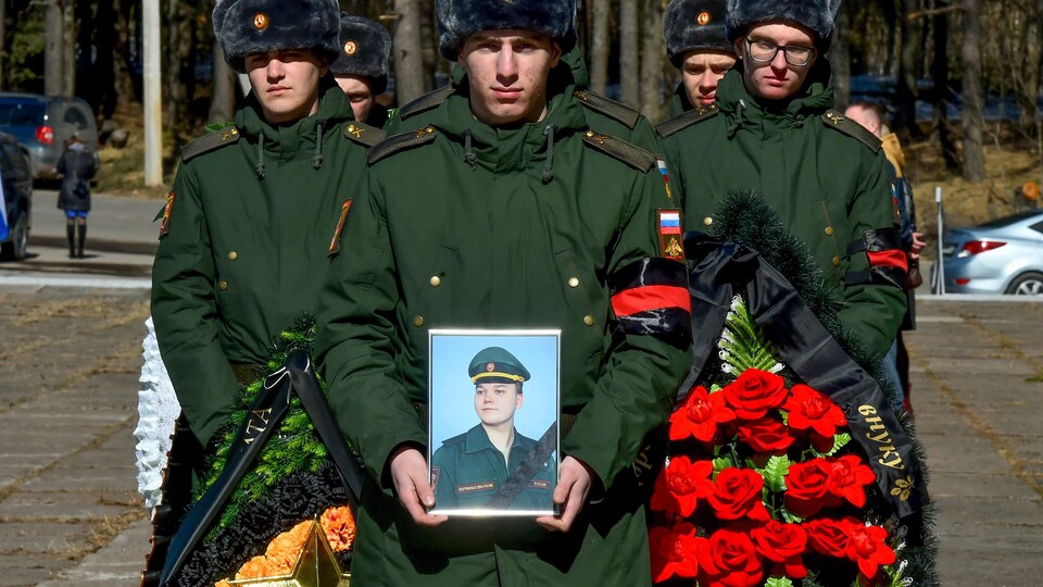 Des soldats russes marchent en rangs. En avant du cortège, un soldat tient une photo du défunt entre ses mains.