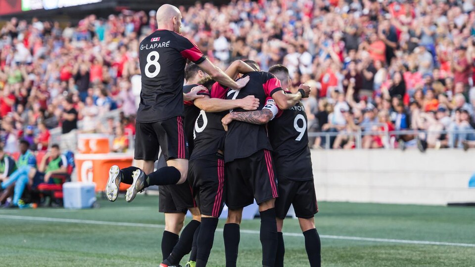 Les joueurs de soccer se sautent dans les bras devant les estrades d'un stade.
