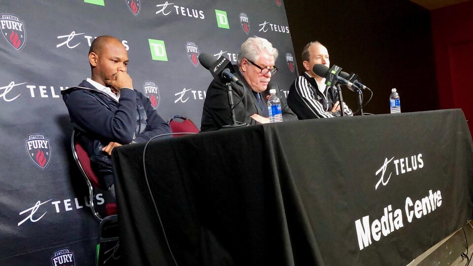 Trois hommes en conférence de presse.