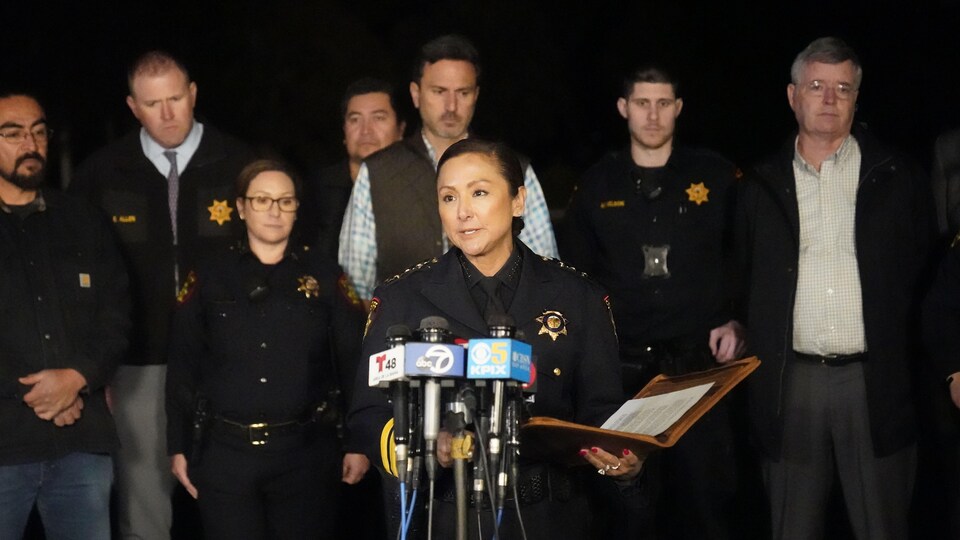 A female sheriff speaks into microphones.  Behind her, police colleagues. 