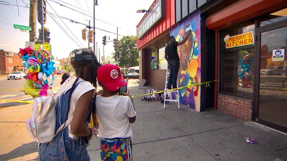 Deux personnes regardent un artiste mettre la touche finale à une œuvre d'art peinte sur un mur.