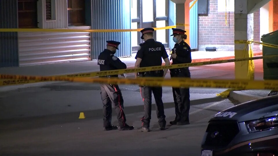 Trois policiers examinent le sol sur une scène de crime.