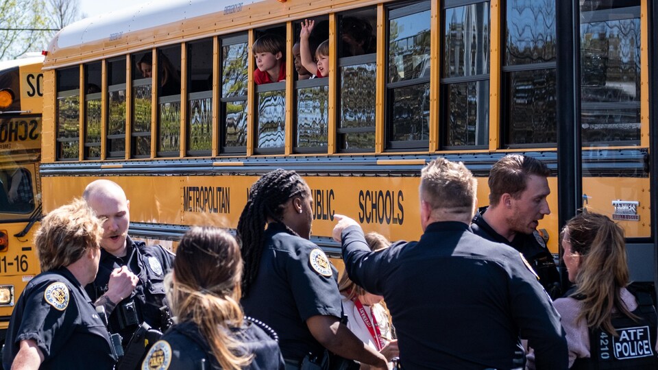 Des enfants regardent par les fenêtres dans un autobus. Des policiers sont debout, à l'extérieur du véhicule.