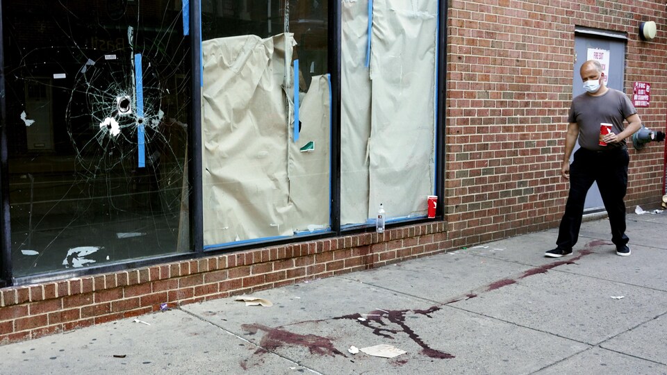 A man was walking on the bloody sidewalk, near the window full of bullets.