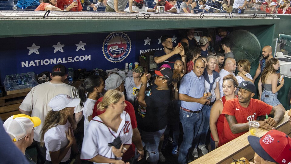 Des spectateurs s'entassent au banc des joueurs dans un stade de baseball.