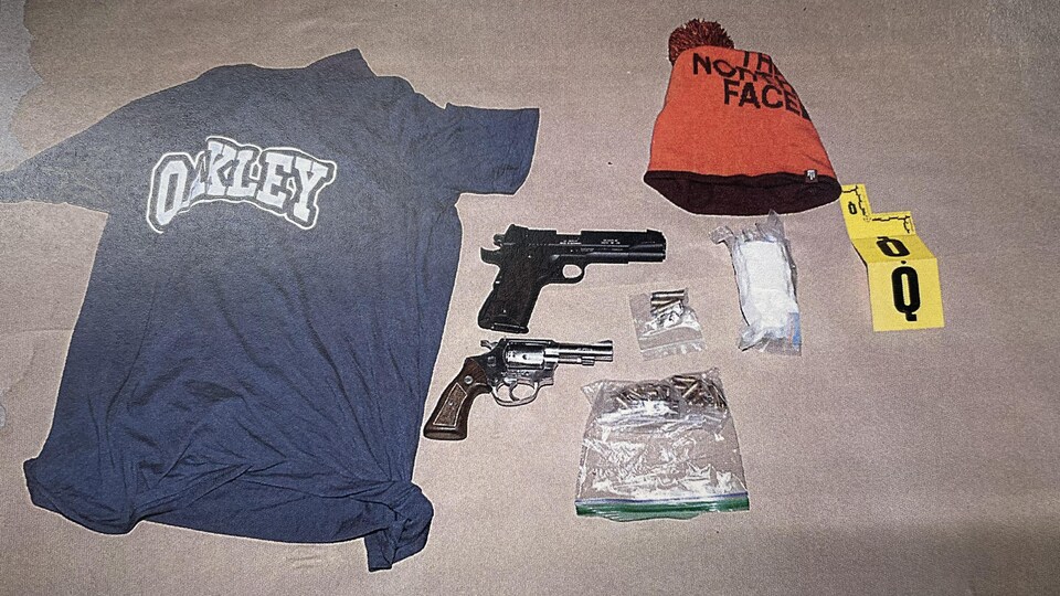 A t-shirt, a toque, two handguns, white powder and rifle cartridges were scattered on Kraft paper.