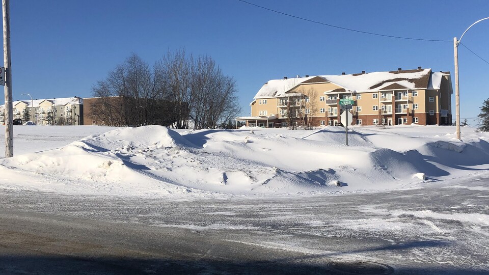 Un terrain enneigé à une intersection avec des immeubles à logement un peu plus loin.