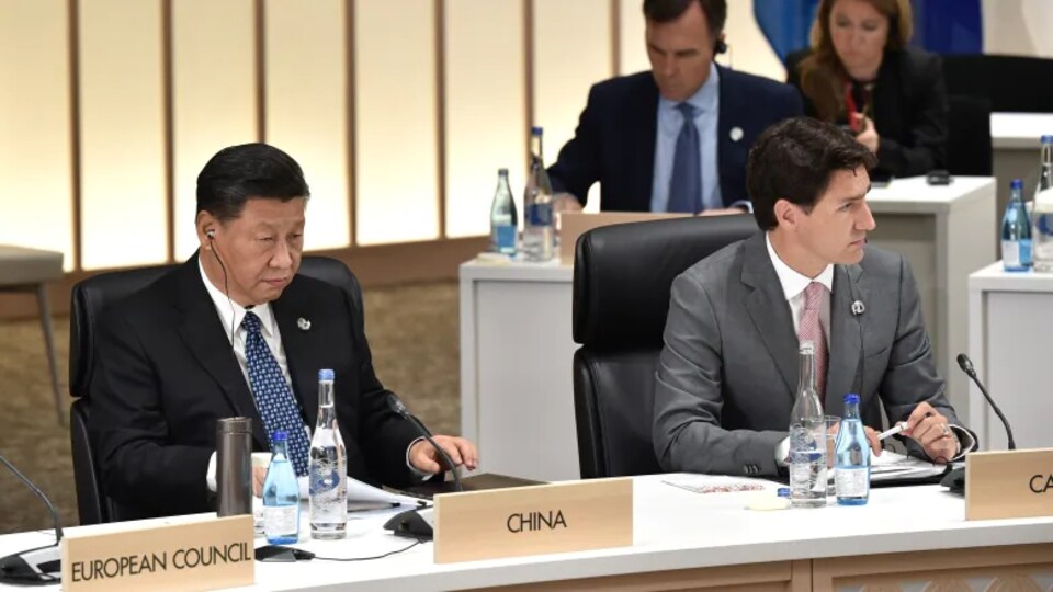 Xi Jinping assis à côté de Justin Trudeau, à une table avec des micros. 