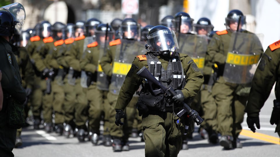 Des policiers en uniforme vêtus de masques à gaz 