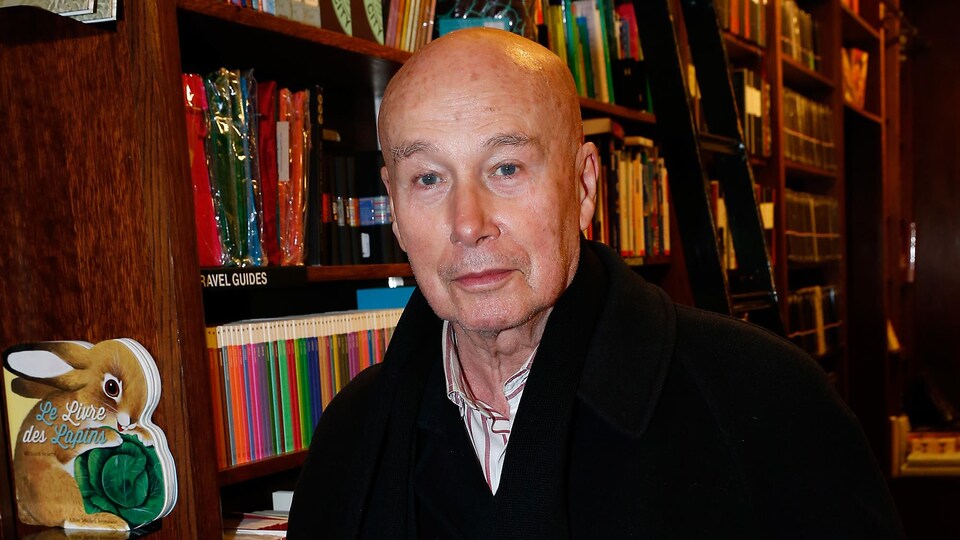 L'homme est debout devant une bibliothèque et tient dans sa main un verre.