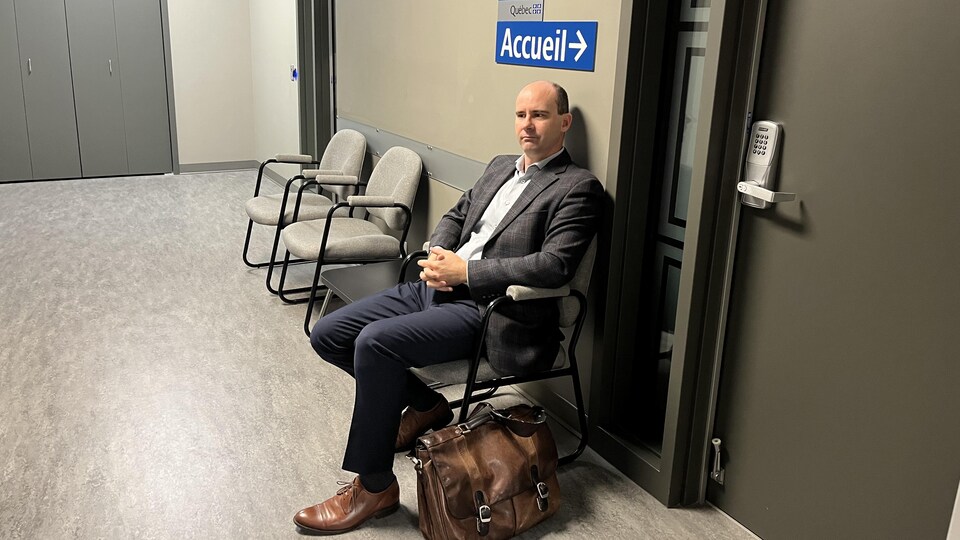 Un homme assis sur une chaise dans un corridor.