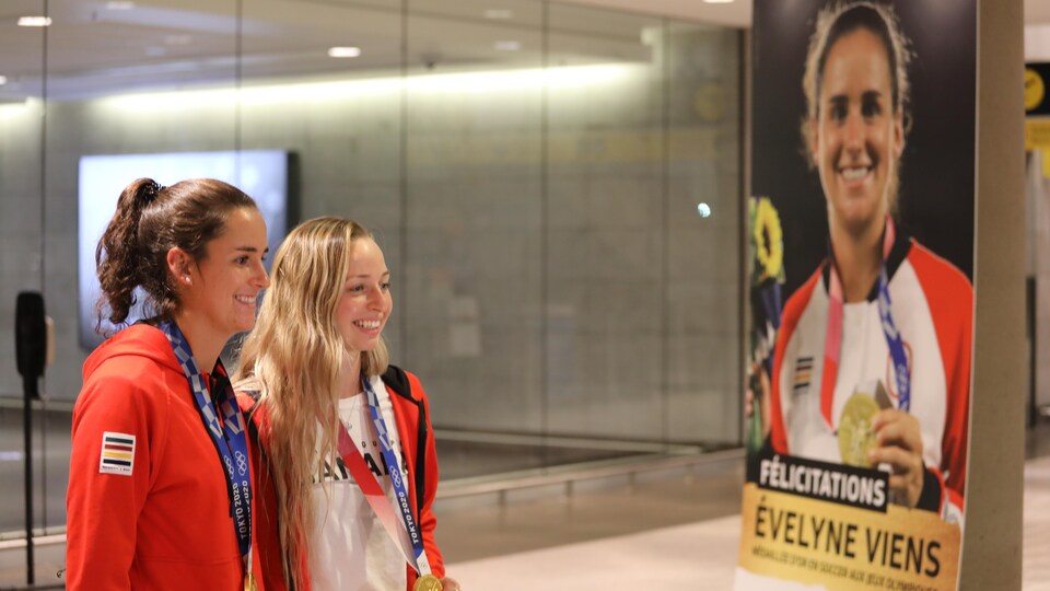 The two players pose in front of a huge poster of Evelyne Viens with her medal on the Olympic podium. 