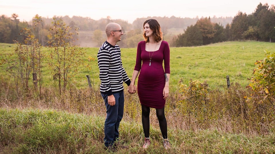 Un homme et une femme enceinte se tiennent par la main devant un champ.