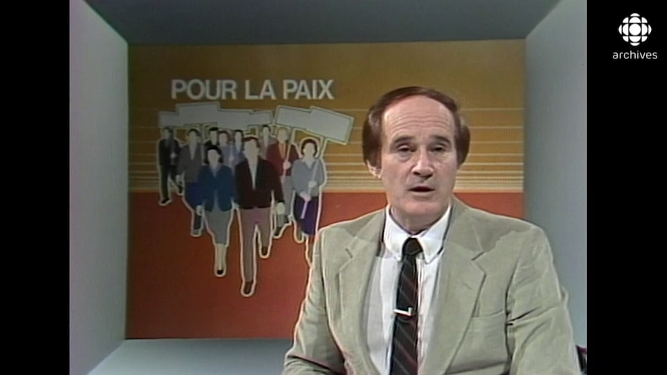 Le présentateur est devant une illustration de manifestants avec l'inscription « pour la paix ».