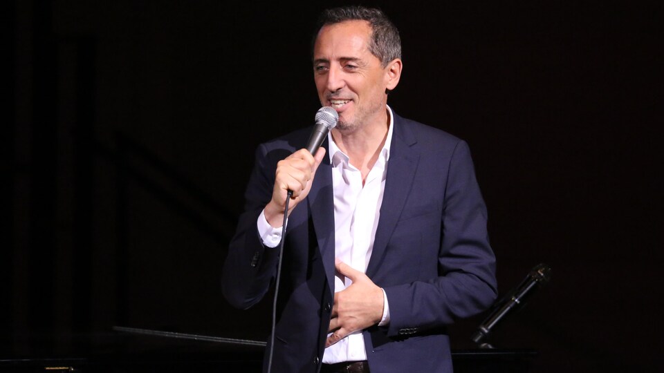 L'homme est sur une scène avec un micro et sourit.