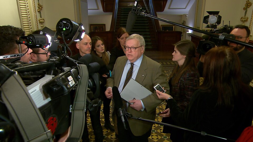 Gaétan Barrette est entouré de journalistes avec leurs micros et leurs caméras.