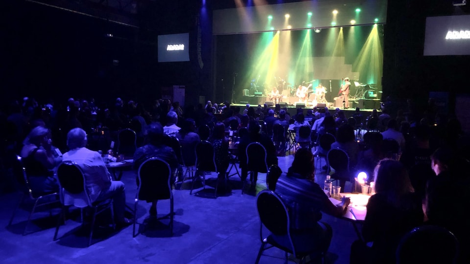 Des personnes assises dans une salle regardent un spectacle de musique sur une scène.