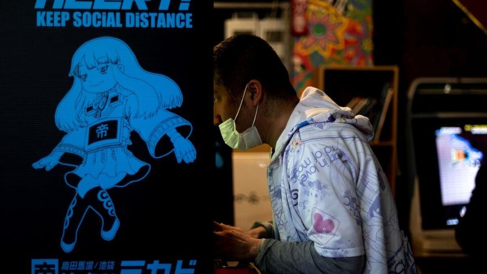 Un homme masqué, au beau milieu d’une partie, dans une salle d’arcade au Japon.