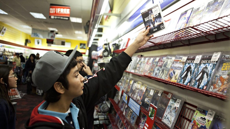 Un jeune prend un jeu sur une tablette d'un magasin de jeux vidéo. 