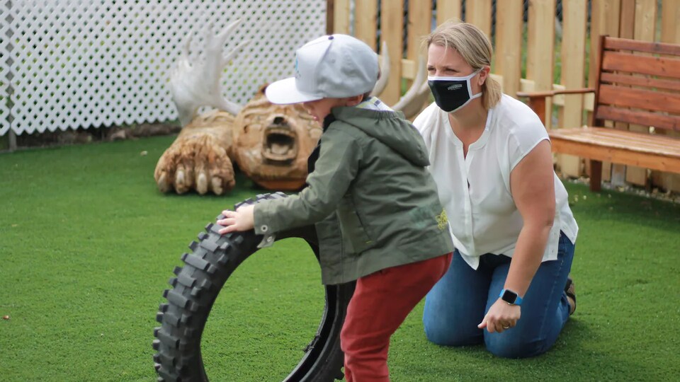Un enfant joue avec un pneu sous la surveillance d'une éducatrice.