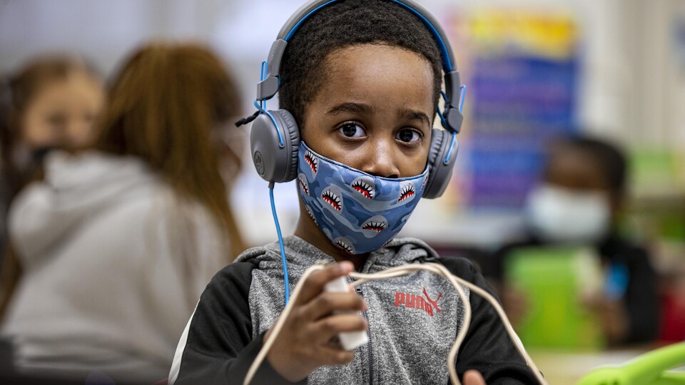 Un enfant qui joue porte des écouteurs et un masque dans un service de garde.