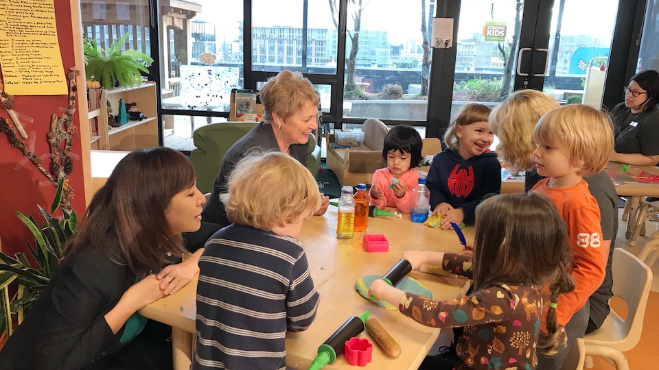 De jeunes enfants et des éducatrices jouent sur une table avec de la pâte à modeler.