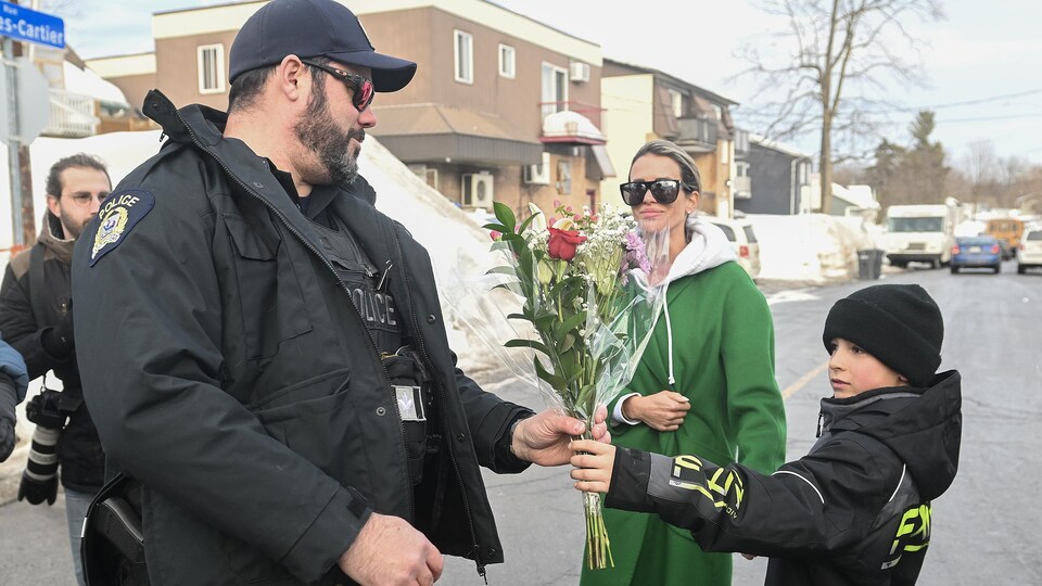Un garçon tend des fleurs à un policier en service qui les prend.