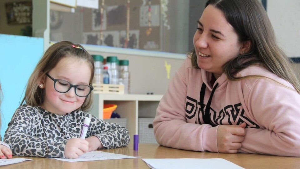 Une jeune femme regarde une fille qui dessine.
