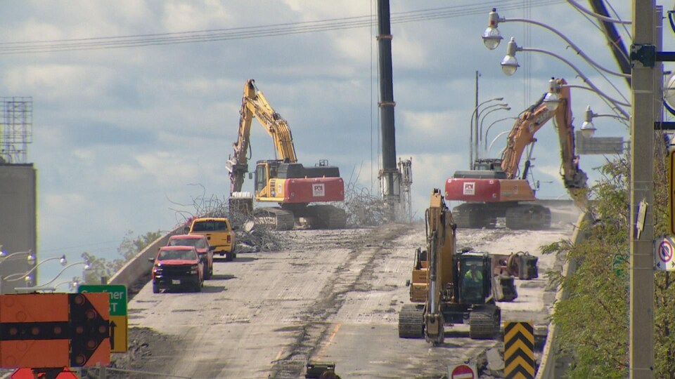 Des équipements lourds et des camions travaillent sur une rampe d'accès en partie détruite.