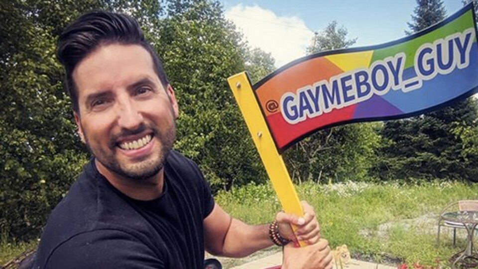 Pascal Lafortune tient un drapeau multicolore où il est écrit Gaymeboy_guy