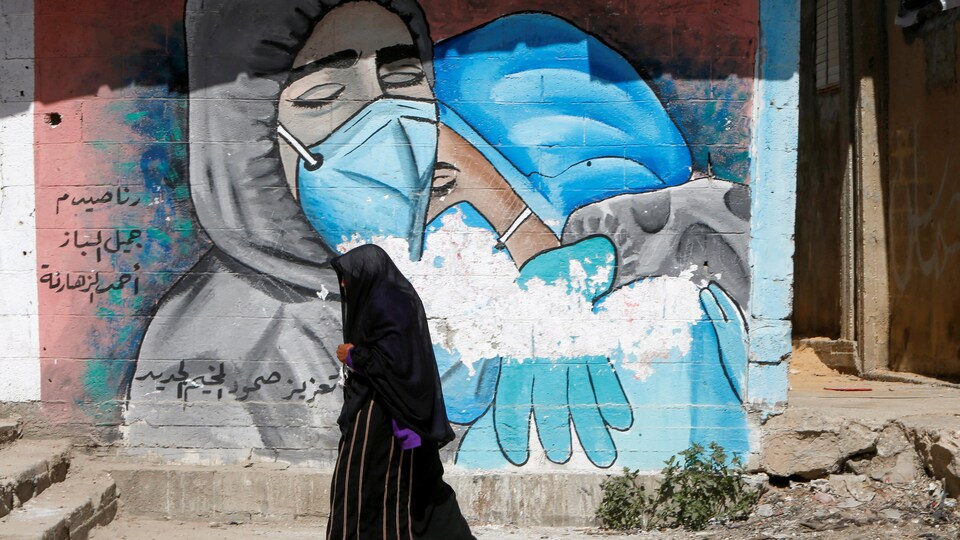Une femme voilée devant une murale de deux infirmières qui se consolent.