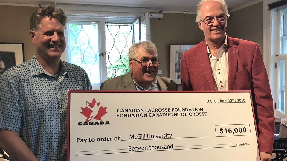 L'entraîneur Tim Murdoch, Jim Calder (Fédération canadienne de crosse) et Marc Gélinas (McGill) posent avec le chèque de 16 000 $ de la Fédération.