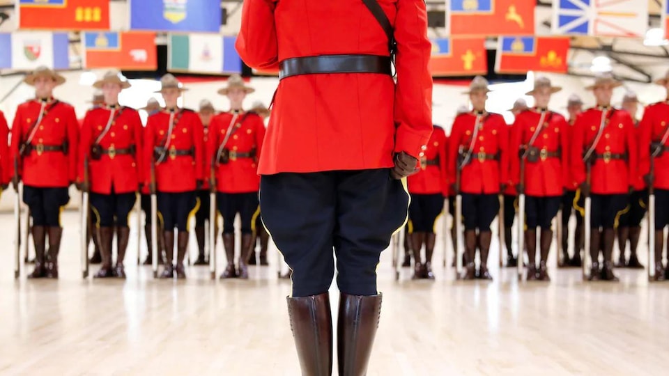 Un officier de la Gendarmerie royale du Canada faisant dos l'objectif, face à un groupe de policiers.