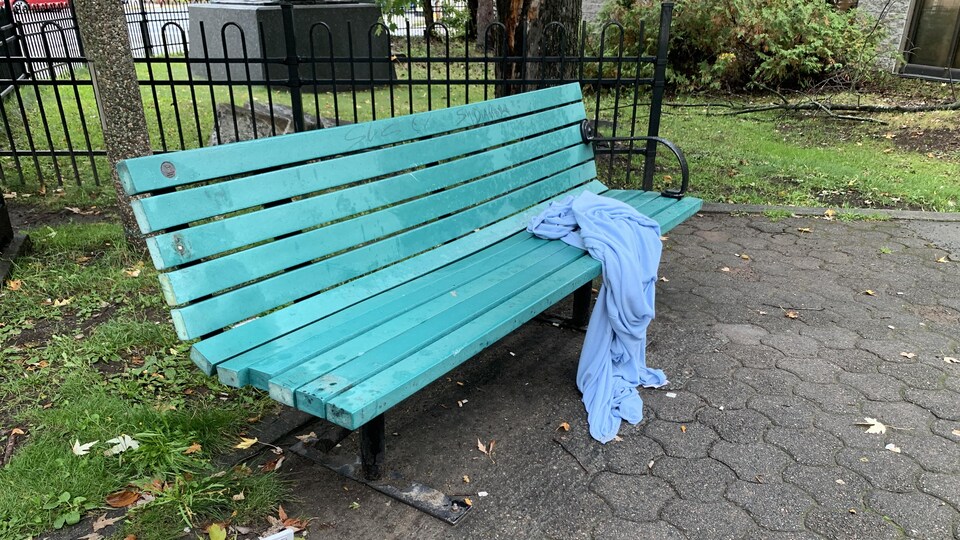 Une couverture dépliée sur un banc de parc touche aussi le sol.