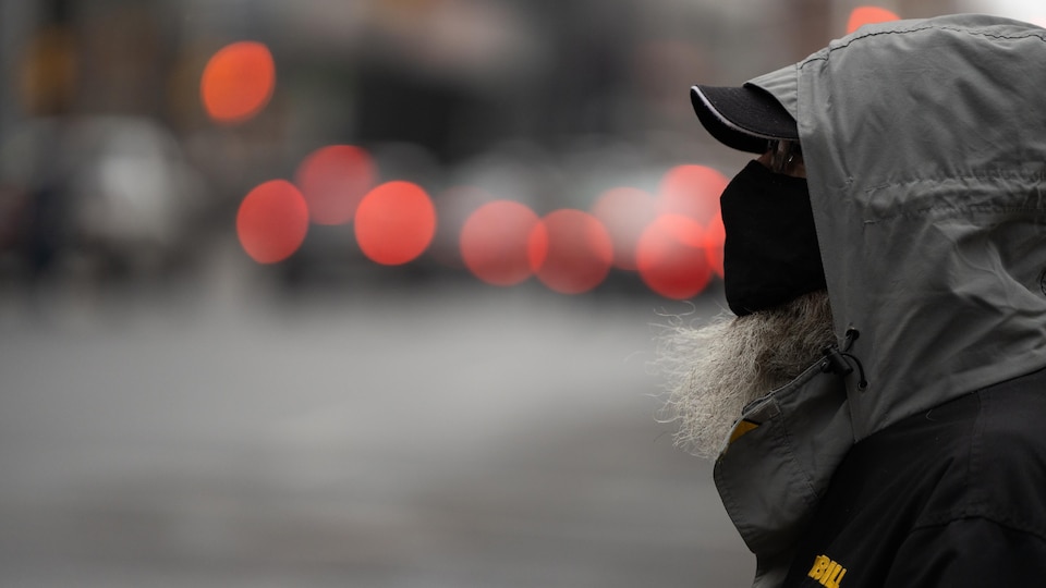 Une personne est debout sur le bord de la rue. Au loin, on distingue à peine les phares de voitures et le reste de la rue.