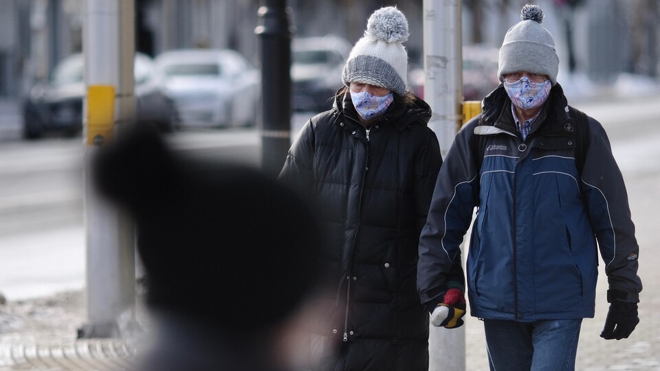 Un couple marche main dans la main dans les rues d'Ottawa. Les deux personnes portent le masque.