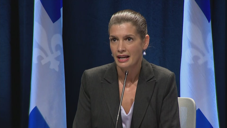 Geneviève Guilbault est assise devant des drapeaux du Québec.