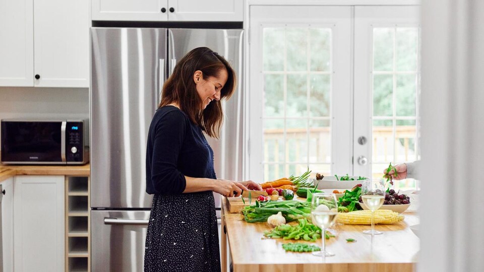 On voit la nutritionniste dans une cuisine aménagée. Elle coupe des légumes frais en souriant.