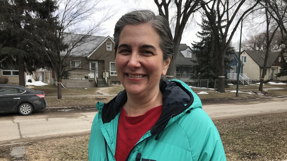 Une femme avec un manteau bleu-vert et un chandaiil rouge, sur le trottoir, dans un quartier résidentiel.