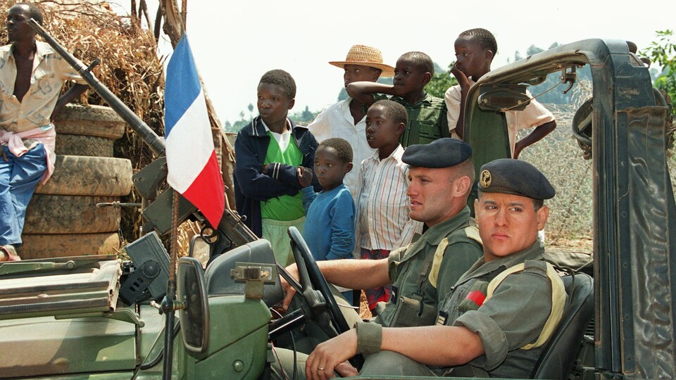Deux soldats sont assis dans un véhicule militaire entouré de Rwandais. 