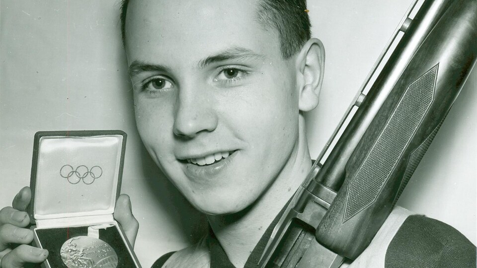 Un homme avec une médaille olympique et un fusil.