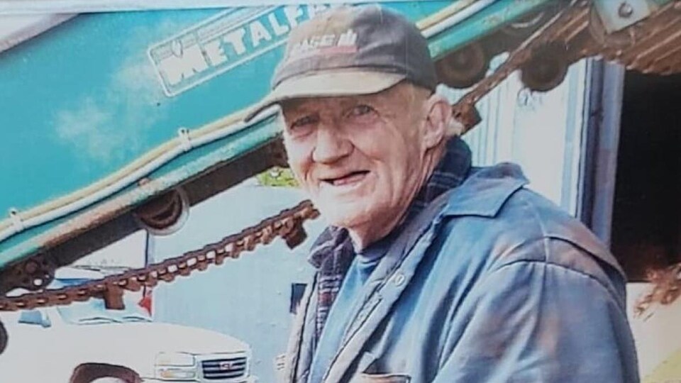 George Kinch pose pour la photo dans une ferme à coté de l'équipement agricole.