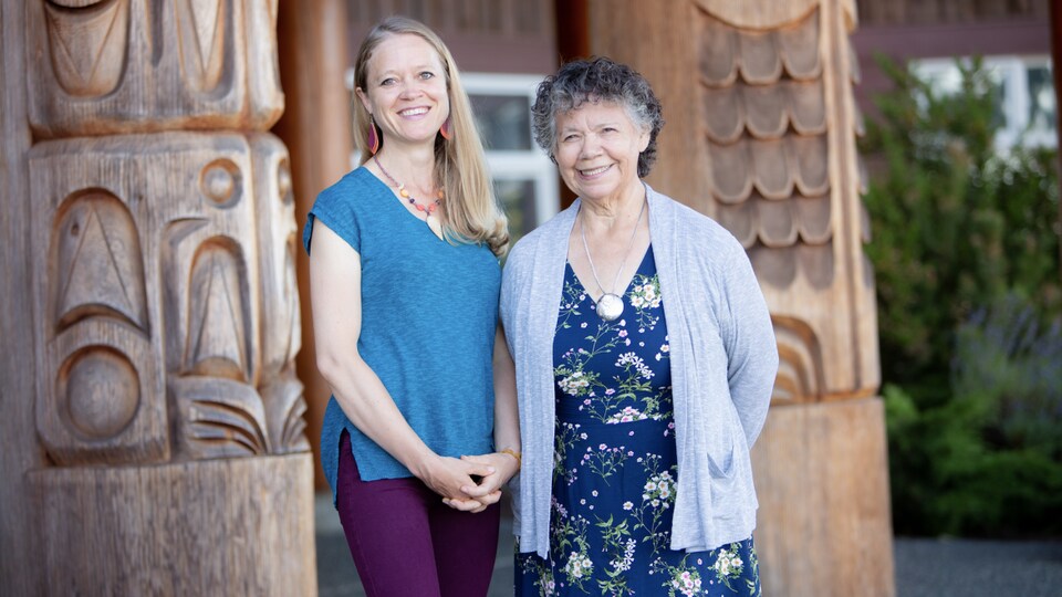 Deux femmes sourient devant un bâtiment de tradition autochtone